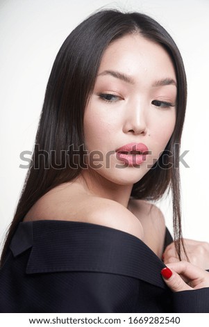  portrait of a young beautiful Asian girl, holding her hands to her chest, looking away, dressed in a blue jacket. The concept of skin care and hair                              