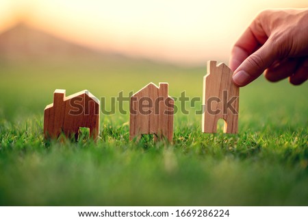 Hand of woman choosing mini wood house model on green grass, Planning buy Real Estate, eco house icon concept.