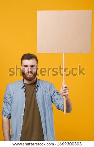 Serious young protesting man guy hold in hand protest sign broadsheet blank placard on stick isolated on yellow wall background studio portrait. Protests strikes pickets concept. Youth against city