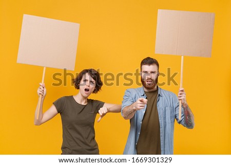 Dissatisfied protesting two people guy girl hold protest signs broadsheet blank placard on stick showing thumb down isolated on yellow background. Protests strikes pickets concept. Youth against city