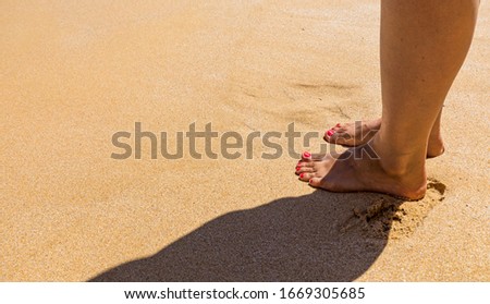 Woman walking barefoot on a beach. Close up leg of young woman walking along wave of sea water and sand on the summer beach. Travel Concept. Woman walking on sand beach leaving footprints in the sand.