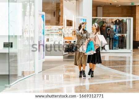 Shopping and entertainment, mall inside. Two beautiful girls with paper bags at the mall. The joy of consumption, Gift shopping, holiday Royalty-Free Stock Photo #1669312771