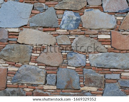 The wall is made of natural blue, red, black, beige and white stone with grey cement mortar. 