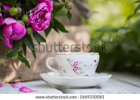 Beautiful bouquet of pink peonies in a vintage box and a cup of tea on a white, wooden table in the garden.