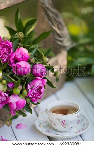 Beautiful bouquet of pink peonies in a vintage box and a cup of tea on a white, wooden table in the garden.