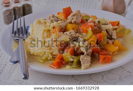 Chicken stew with creamed mashed potatoes,shot close up and from slightly above,there is a white lace table cloth.