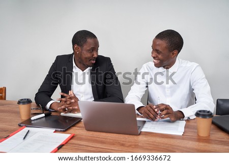 Laughing African American businessmen discussing paperwork with a coworker at a table in an office
