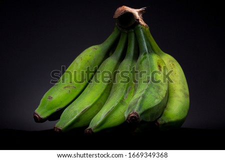 Bundle of brightly lit vibrant green bananas on a black surface with dark grey studio background