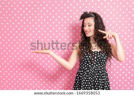 Lady in pin-up style keeping palm open for text or product, looking and pointing finger at it.