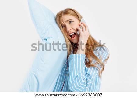 Annoyed disgruntled young girl in pajamas talking on the phone on a white background