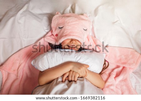 Top view of cute awaking school girl with her toy animals wearing in light pink pajama with unicorn hoody, happy family concept, indoor horizontal portrait