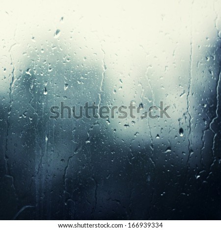 Rainy drops on the glass with the dark blue blurry background
