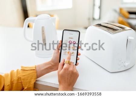 Controlling smart kitchen appliance using mobile phone at home, close-up on mobile screen. Concept of a smart home devices Royalty-Free Stock Photo #1669393558
