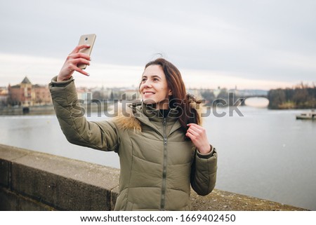 Happy young woman takes selfie portrait on Charles Bridge, Prague, Czech Republic. Pretty tourist make funny photos for travel blog in Europe. Woman Taking A Selfie In Prague.