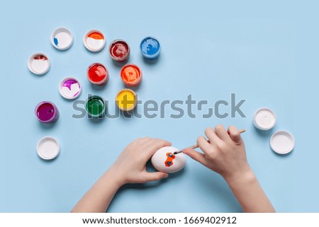 A child paints a white egg. Top view, place for your text.