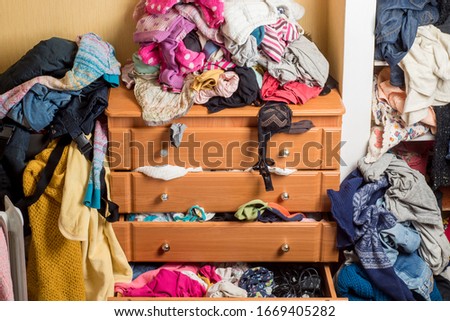 open chest drawers with drop-down clothes and piles of clothes around in a mess.Close-up Royalty-Free Stock Photo #1669405282