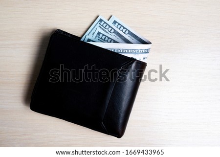 bundle of dollar bill in black leather wallet on a light wooden background. view from above. to close