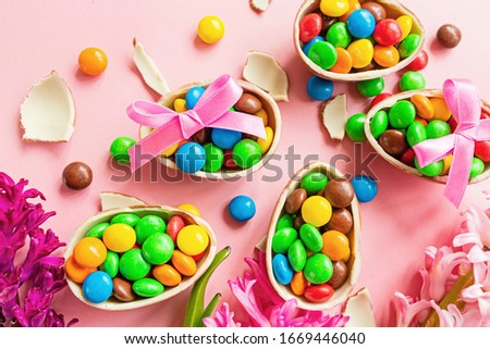 Chocolate Easter eggs and colorful candies on pastel pink paper background. flat lay, top view, overhead, template, mockup