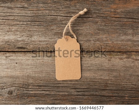 Empty brown paper tag tied with white string. Price tag, gift tag, sale tag on the gray wooden background, close up