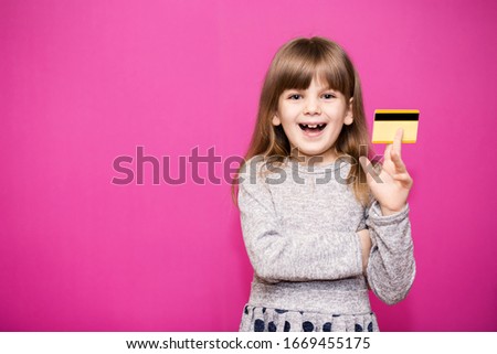 Happy little girl holding new bank credit card and ready to go shopping isolated on pink background