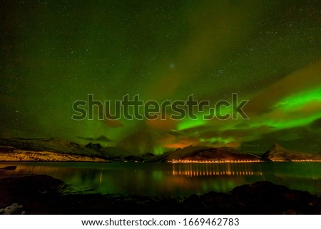 Aurora borealis, polar lights, northern lights, over fjord mountains with many clouds and stars in the sky in the North of Europe , Lofoten islands, Norway, long shutter speed.