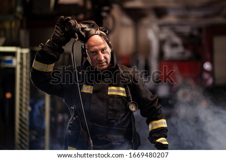 firefighter portrait wearing full equipment and emergency rescue equipment. taking off oxygen mask all sweaty after successful intervention. smoke and fire trucks in the background.