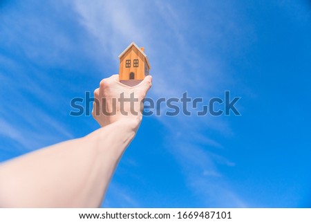 Male hand holds wooden house on blue sunny sky background.  Image of buying a house.