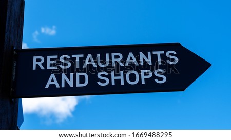 A signpost pointing to restaurants and shops, isolated against a cloudy blue sky