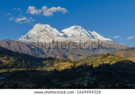 Huascaran mountain in Peru with its two snowy peaks rising over green valley where the town of Yungay sits, destroyed by a flood