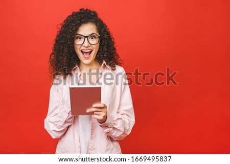 Excited amazed young beautiful woman with tablet pc. Happy girl in white shirt using tablet computer, isolated on red background. 