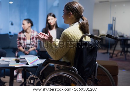 Handicapped young woman with colleagues working in office. She is smiling and passionate about the workflow. Performing in co-working space. Office people working together. Royalty-Free Stock Photo #1669501207