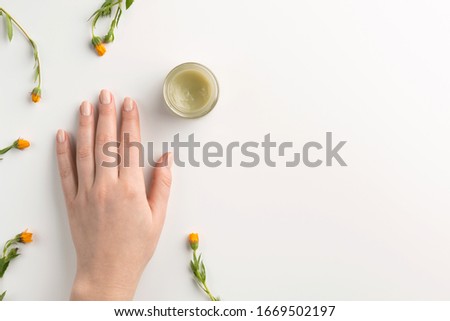 Organic cosmetic concept. Flowers of calendula, female hand and cosmetic cream isolated, on white background. Flat lay, top view, copy space.