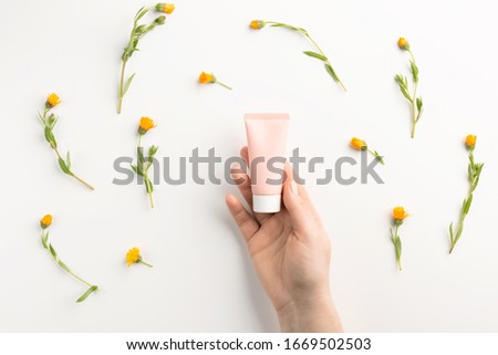 Organic cosmetic concept. Female hand holding tube of cosmetic cream, isolated on white background. Flat lay, top view, copy space.