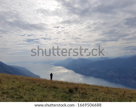 View from Monte Baldo/ Mount Baldo over Lago di Garda / Lake Garda and a man's silhouette. Clouded sky. Holiday destination. Hiking. Solitary. Solitude. Background.