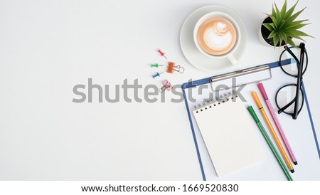 Flat lay education and business concept on white table desk background with blank notepad and highlight marker pen, plant, coffee cup, glasses, stationary, Top view with copy space