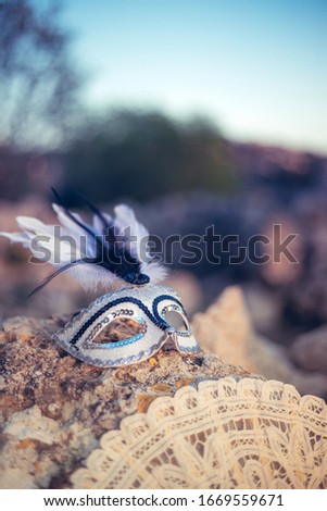 White carnival mask with feathers, a white lace fan on the outdoor nature background