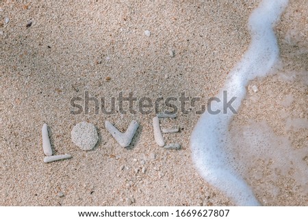 Alphabet "LOVE" by coral fragments on sand and wave in summer season love sea concept