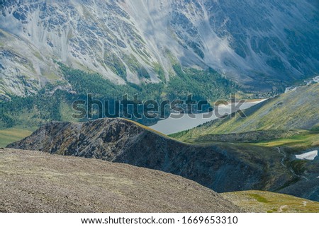 Atmospheric alpine landscape with beautiful valley with mountains lake and giant textured slopes with nature patterns. Awesome aerial view to big rocky hills and huge mountains. Forest on mountainside