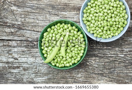 Peas in a bowl with fresh cut plant leaf nearby and bean pods on wooden rustic textured background, closeup, flat lay, from above overhead top view, vegan food and healthy organic food concept