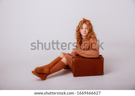 teenage girl sitting next to an old suitcase on a white background