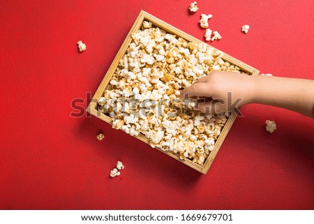 Fresh popcorn spilled out of the  box on a red background. Cinema snack concept. The food for watching a movie and entertainment. Copy space for text, flat lay.