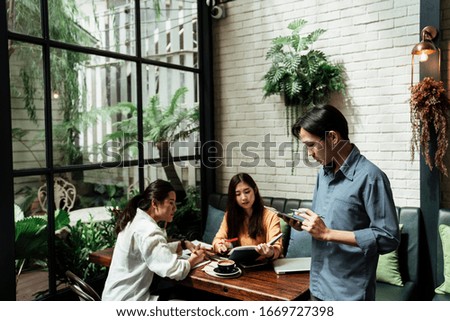 Three young asian business people using tablet in the meeting to explain their business concept and idea. The meeting taking place in cafe. Young business boy making presentation to their colleagues.
