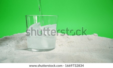 glass with ice and soda water on the sand on a green background