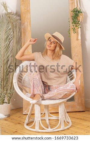 A girl in pajamas sits in a round chair in white hat. She stands in front of a mirror with hands up. Soft pink creamy colors of the picture