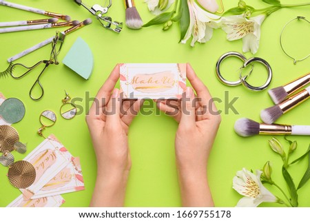 Female hands with business card of makeup artist on color background