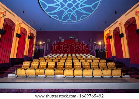 Large cinema theater interior with seat rows for audience to sit in movie theater premiere by cinematograph projector. The cinema theater is decorated in classical for luxury feel of movie watching. Royalty-Free Stock Photo #1669765492