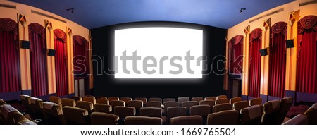 Cinema theater screen in front of seat rows in movie theater showing white screen projected from cinematograph. The cinema theater is decorated in classical style for luxury feeling of movie watching. Royalty-Free Stock Photo #1669765504