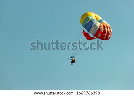 Multicolored parachute against the blue sky. Happy couple Parasailing in summer. Couple under parachute hanging mid air. Having fun. Tropical Paradise. Positive human emotions and feelings in a family