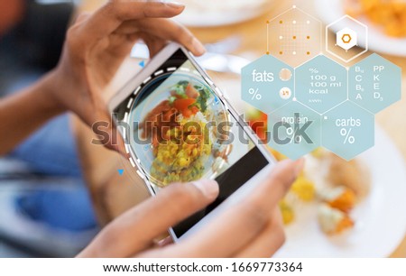 technology, eating and people concept - close up of hands with food on smartphone screen at restaurant over nutritional value chart