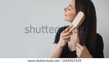 Young beautiful happy woman brushes her long healthy hair with wooden hairbrush on white background. Place for text. Royalty-Free Stock Photo #1669823104